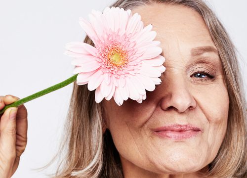 Older woman holding up a flower to her eye